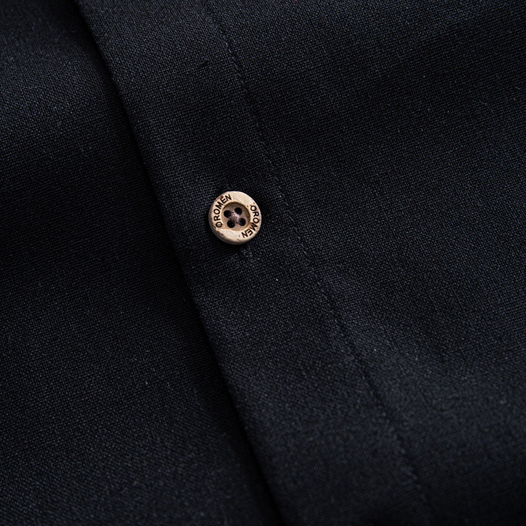 Button detail on men's black linen-cotton long-sleeve shirt, OROMEN natural coconut buttons