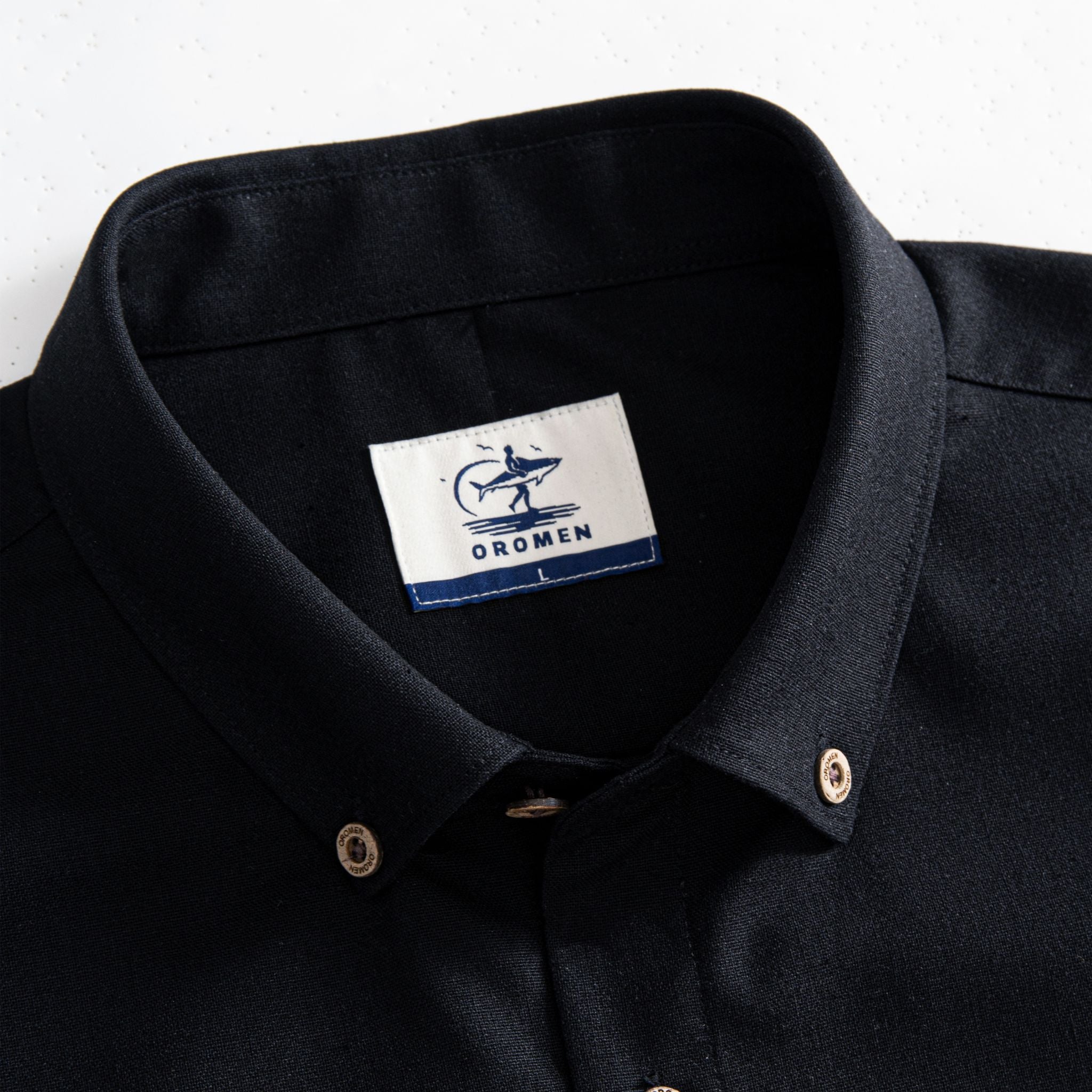 Close-up of OROMEN branded natural coconut button on black linen-cotton shirt fabric
