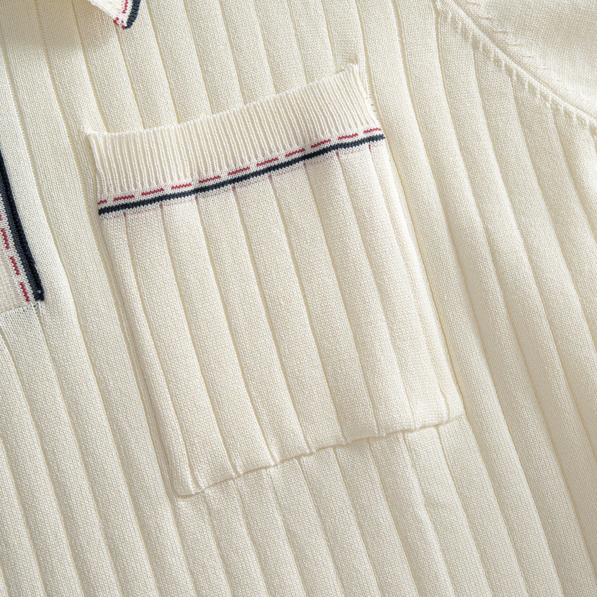 Left chest patch pocket close-up on OROMEN cream ribbed knit polo,
contrast stripe tipping along pocket edge, fine rib texture