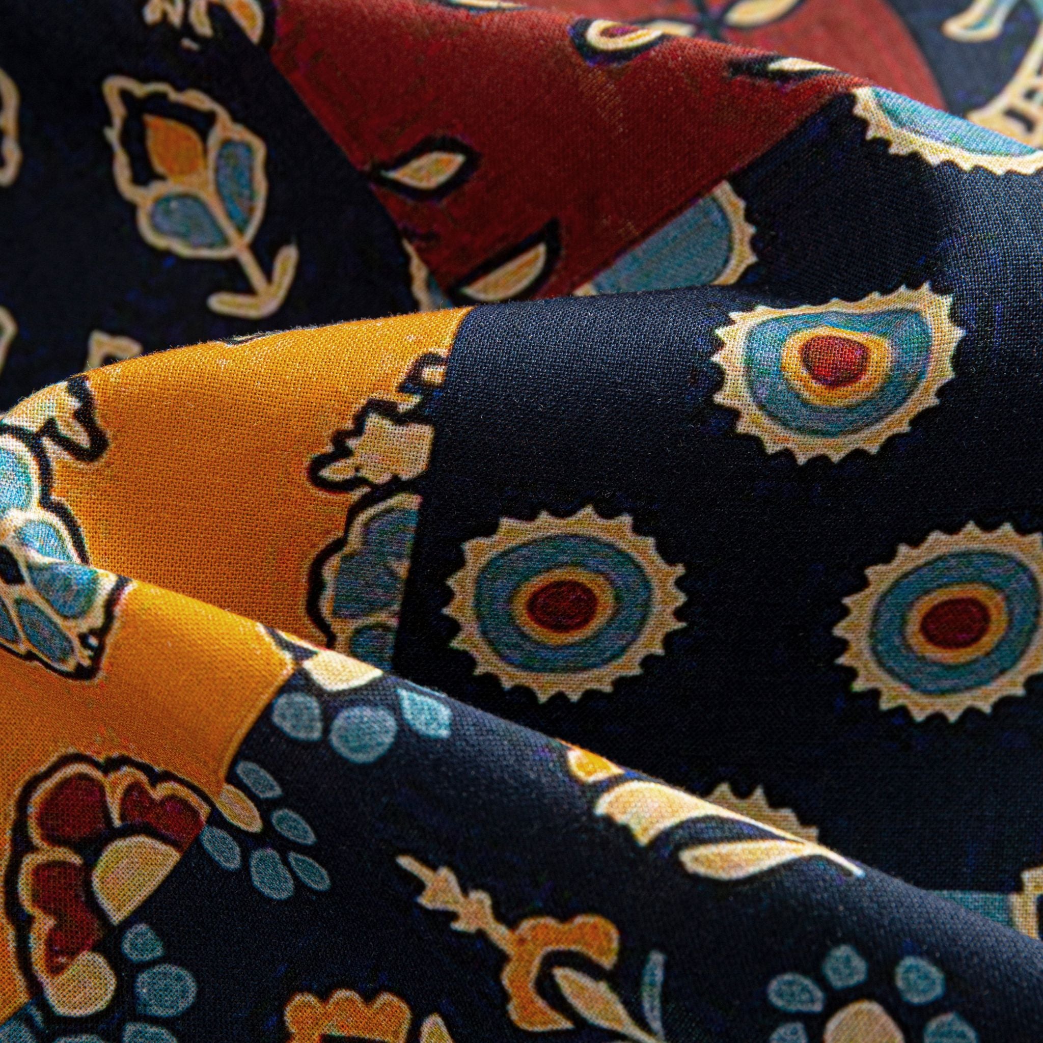 OROMEN Ajrakh Mosaic shirt fabric close-up showing concentric sun circles, paisley and floral patchwork panels in navy, amber and burgundy on 100% premium cotton