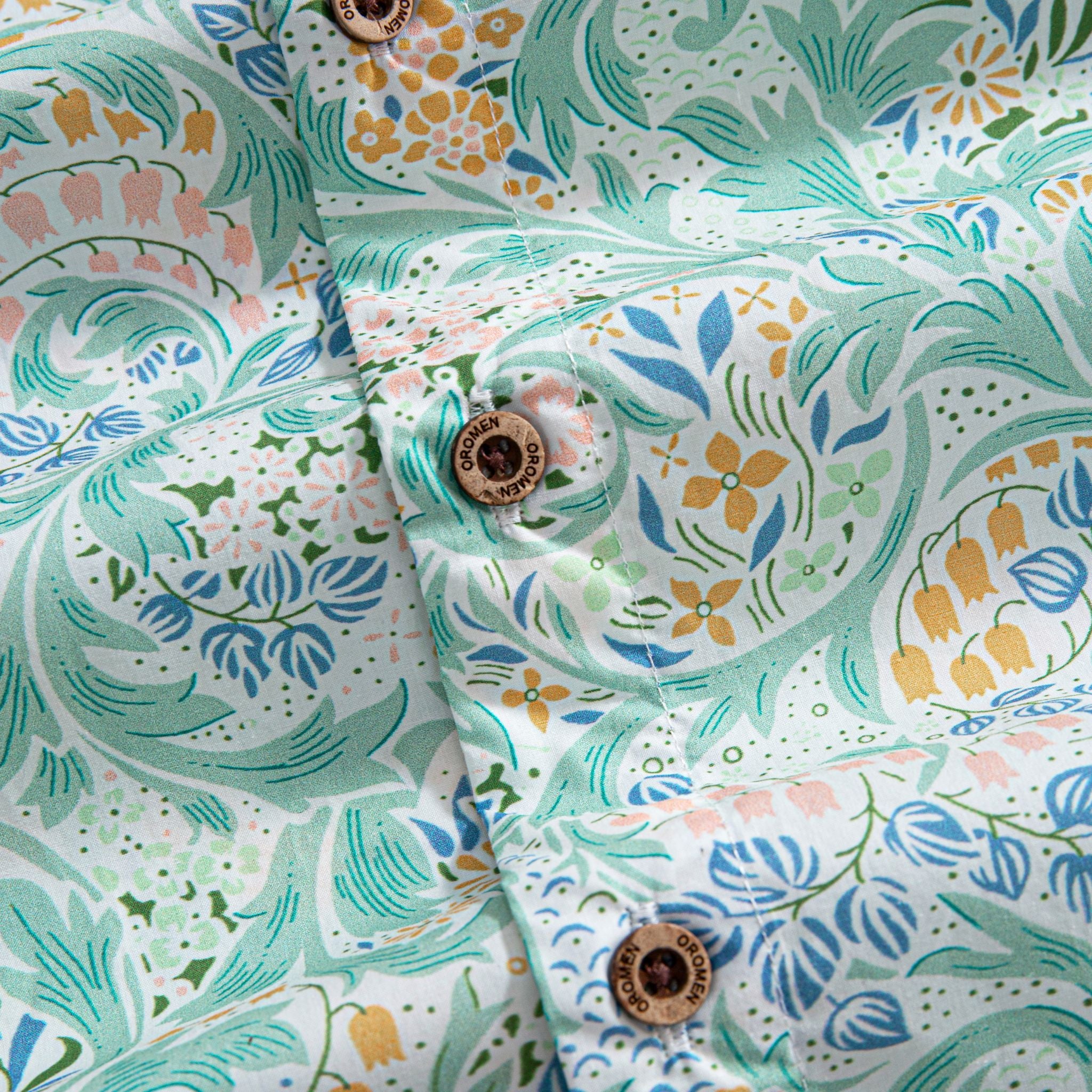 OROMEN Rococo Bloom Hawaiian shirt – engraved coconut buttons close-up with mint Baroque scroll and floral print background