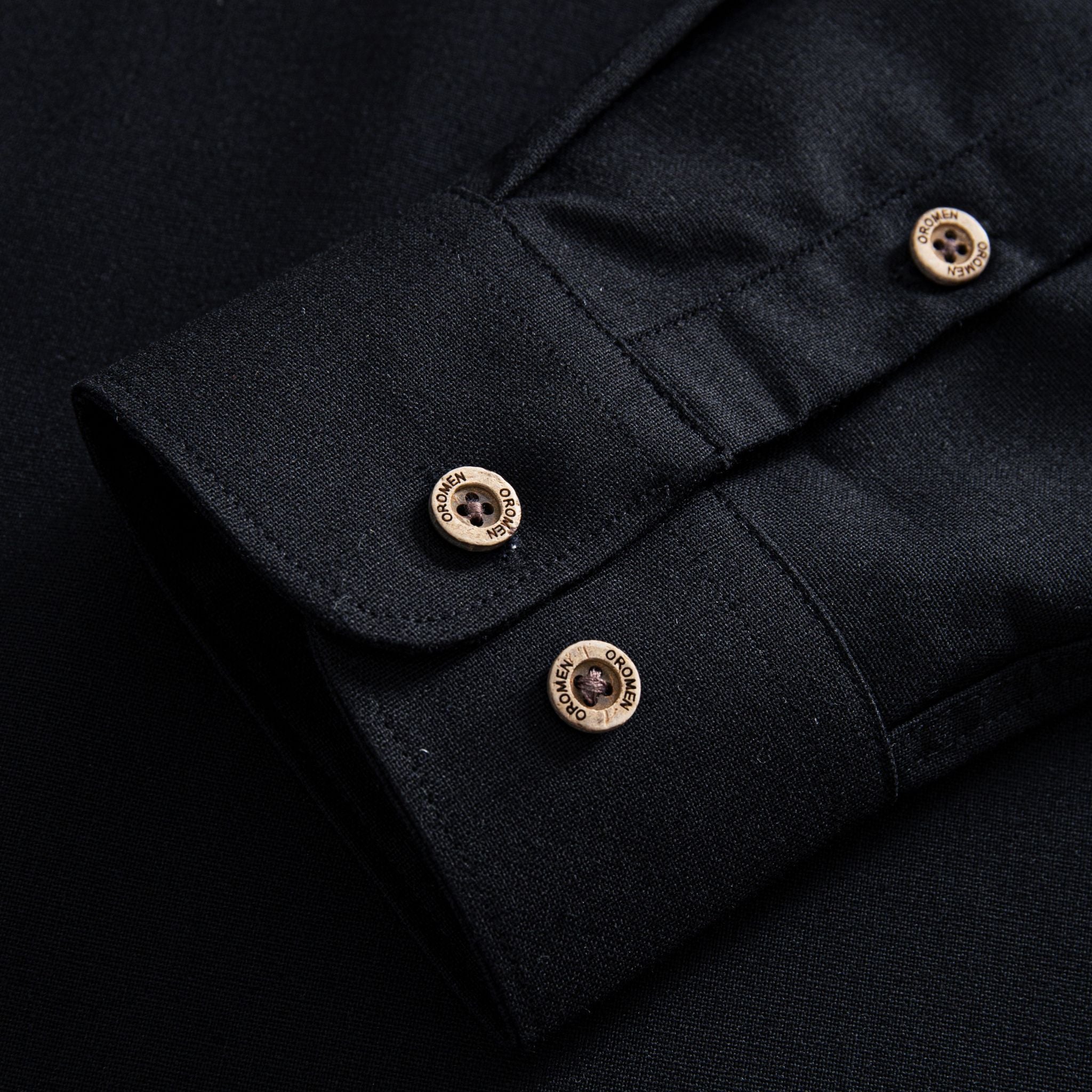 Cuff detail with OROMEN branded coconut buttons on black linen-cotton woven shirt