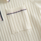 Left chest patch pocket close-up on OROMEN cream ribbed knit polo,
contrast stripe tipping along pocket edge, fine rib texture