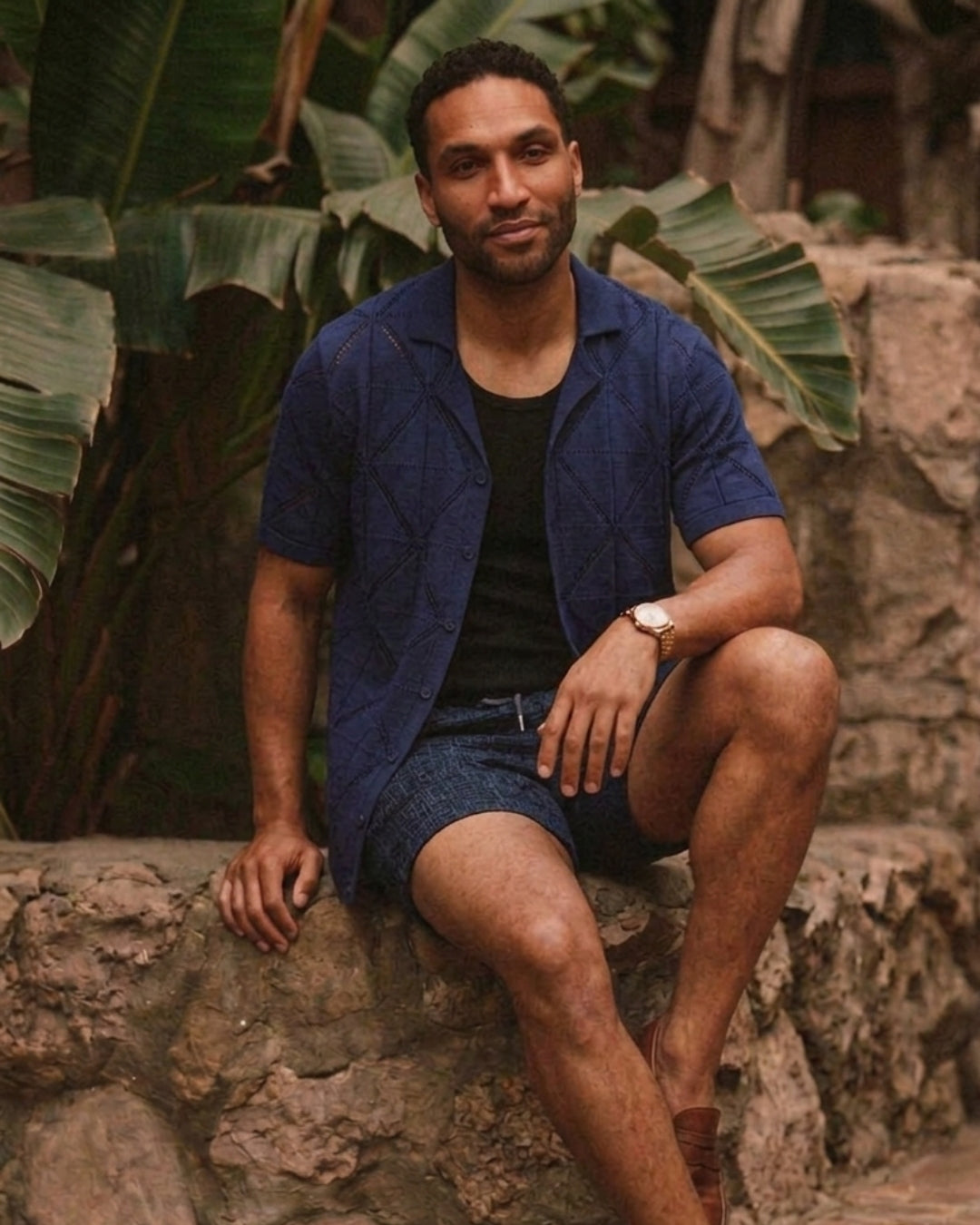 Man in navy geometric open-knit shirt sitting on stone wall