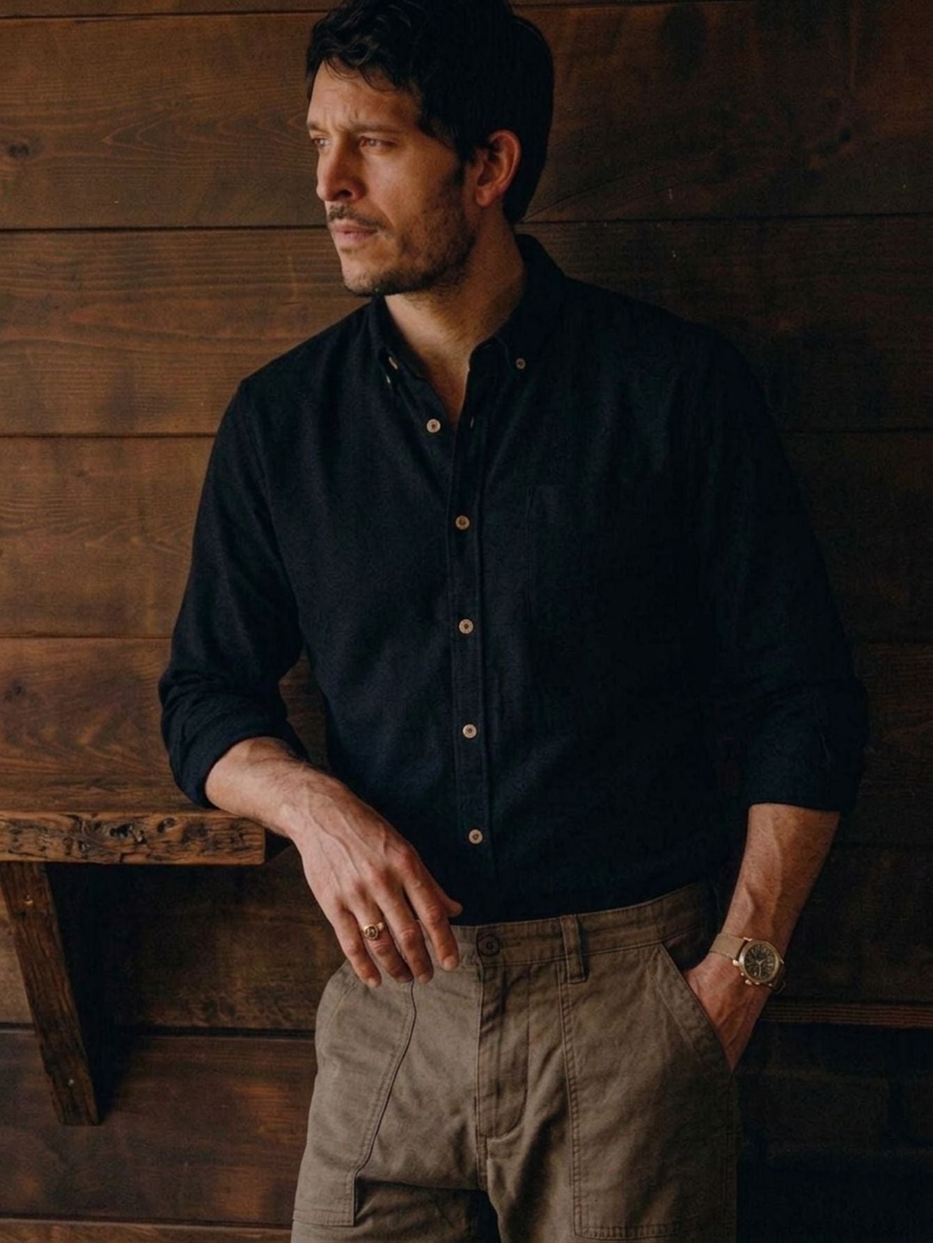 Man wearing OROMEN black long-sleeve linen-cotton shirt with khaki trousers in rustic wood interior