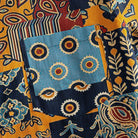 OROMEN Ajrakh Mosaic shirt chest pocket close-up showing slate blue panel with concentric sun circle motifs surrounded by paisley and stripe patchwork blocks
