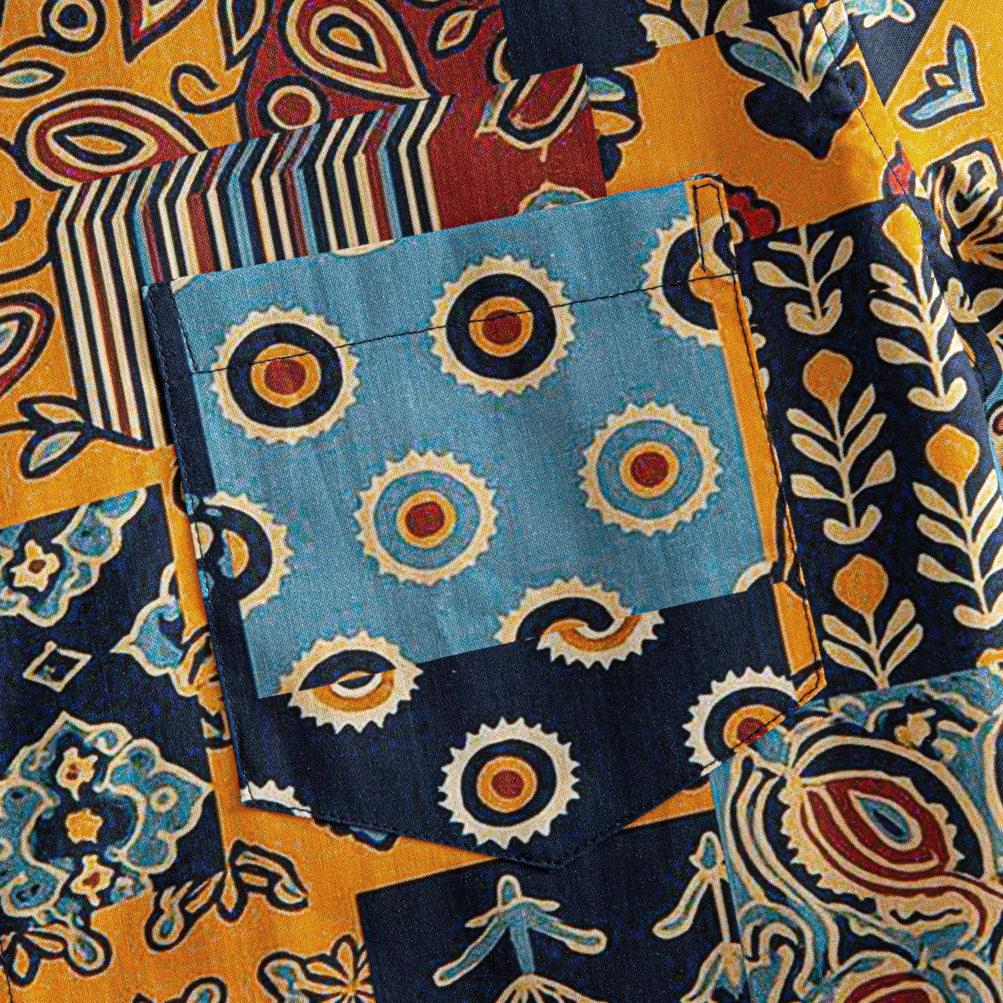 OROMEN Ajrakh Mosaic shirt chest pocket close-up showing slate blue panel with concentric sun circle motifs surrounded by paisley and stripe patchwork blocks