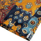 OROMEN Ajrakh Mosaic shirt side vent detail showing multi-color patchwork blocks in navy, amber and slate blue with floral and botanical motifs and double needle stitching