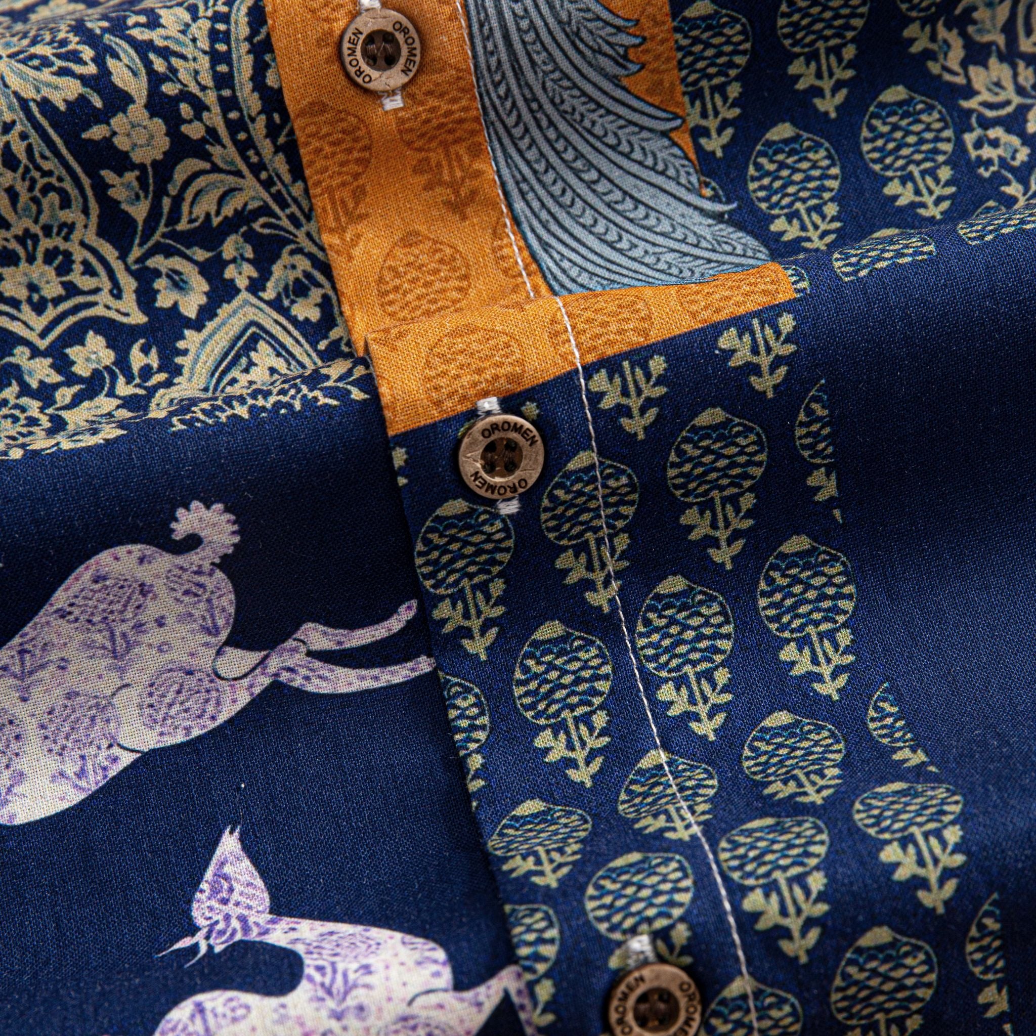 OROMEN Aviary Patchwork shirt branded coconut button close-up against peacock and botanical patchwork panels with amber orange placket