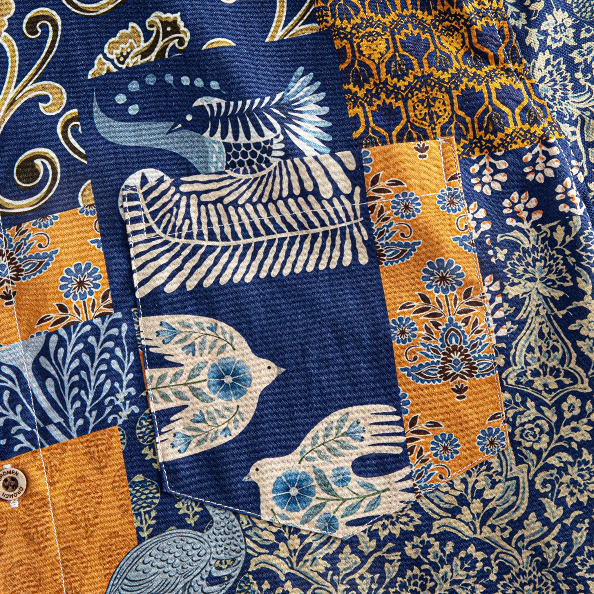 OROMEN Aviary Patchwork shirt chest pocket close-up showing patchwork panel arrangement with peacock and botanical motifs in navy blue and amber orange