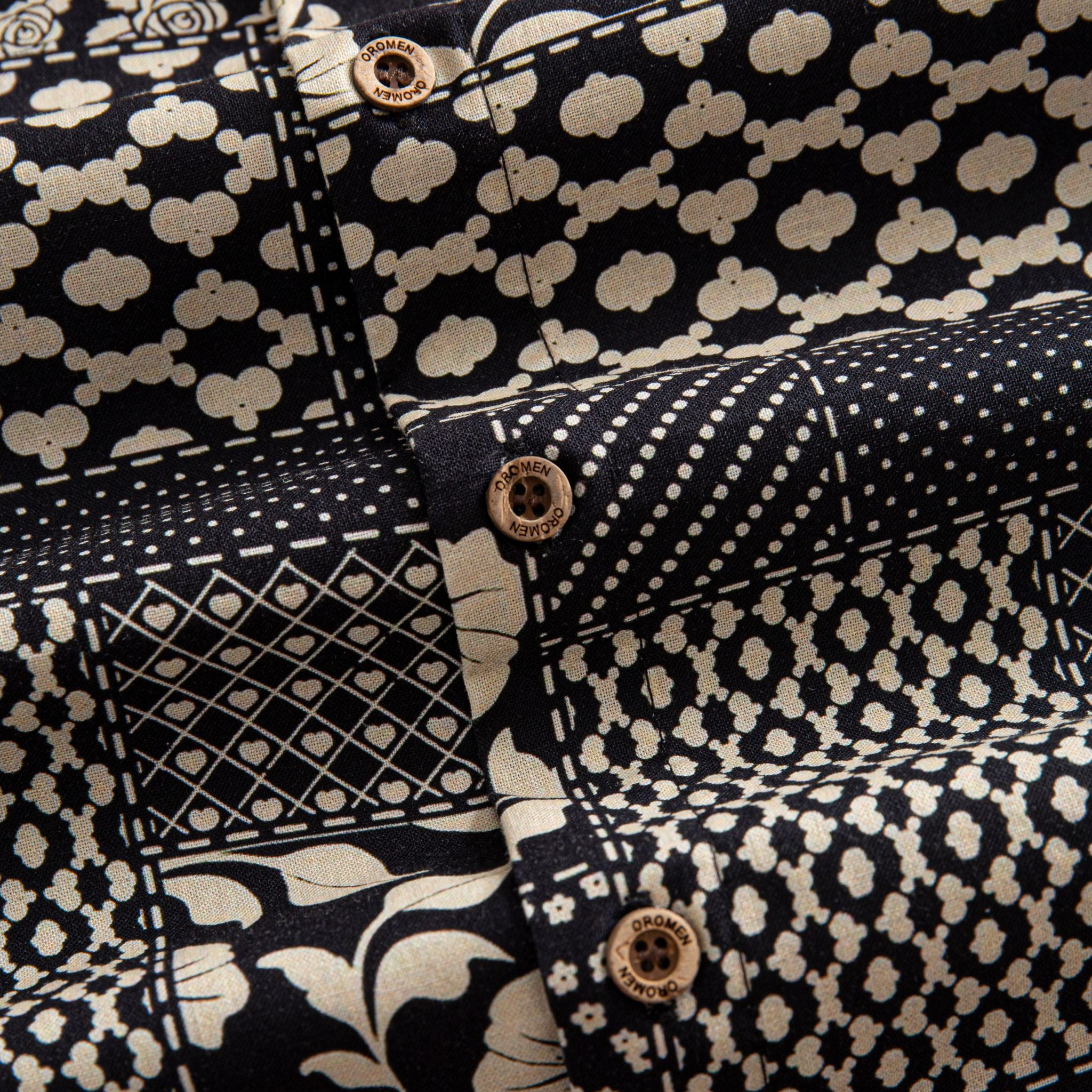 OROMEN Noir Patchwork shirt branded coconut button close-up against leopard spot, diamond heart grid and polka dot patchwork panels in black and off-white