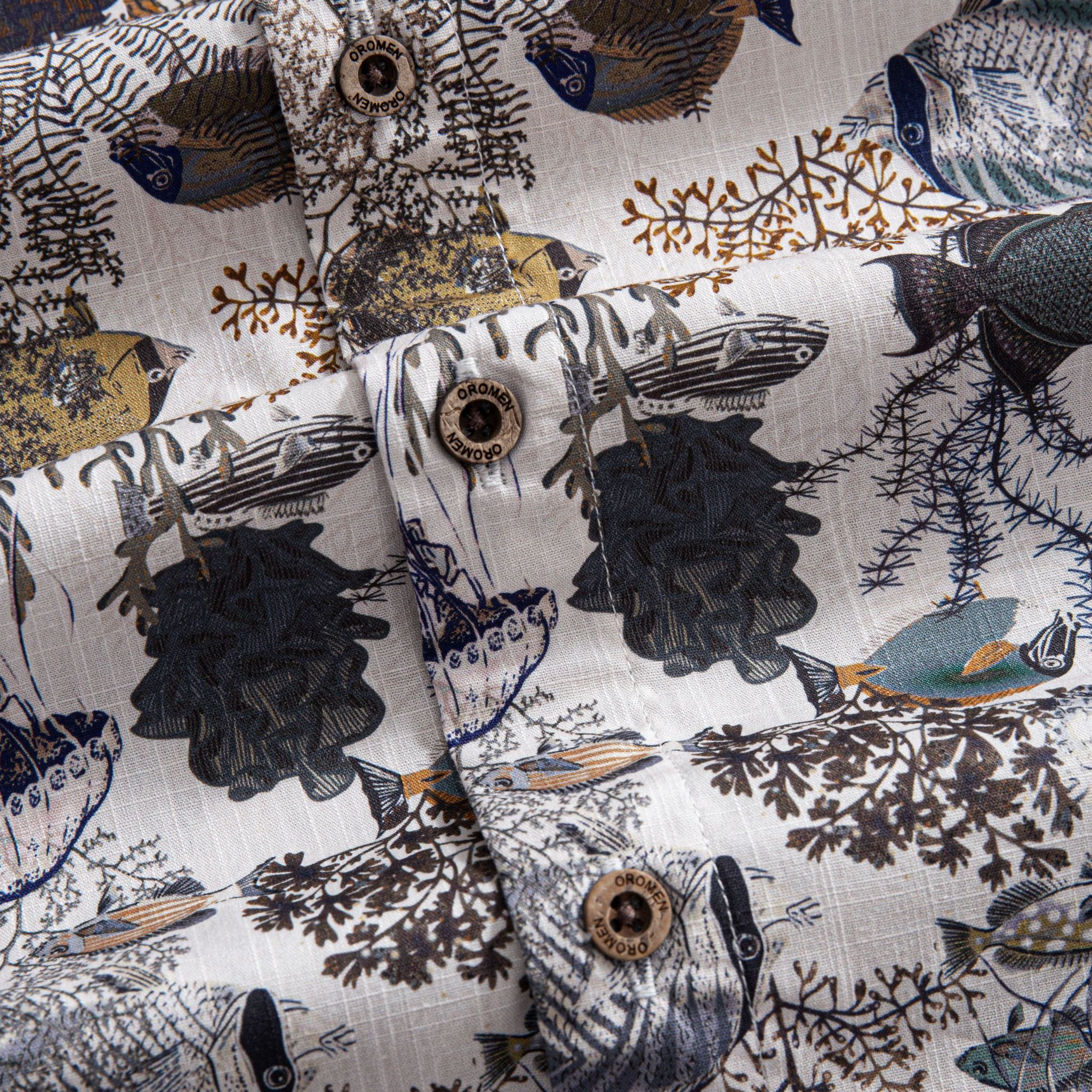 OROMEN Reef Atlas Hawaiian shirt – engraved coconut buttons close-up with marine coral and fish print background