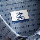 OROMEN Sashiko Chambray shirt branded woven label close-up inside collar, navy Sashiko stitch background