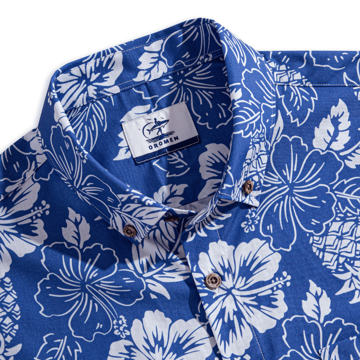 OROMEN Tropical Paradise shirt – collar close-up with OROMEN brand label featuring surfer logo, button-down collar open, coconut buttons on navy blue ground with white hibiscus floral print