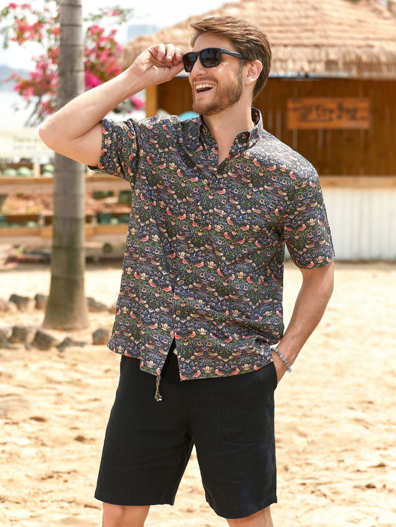 OROMEN men's dark floral Hawaiian shirt featuring bird and strawberry print, worn by a smiling man on the beach