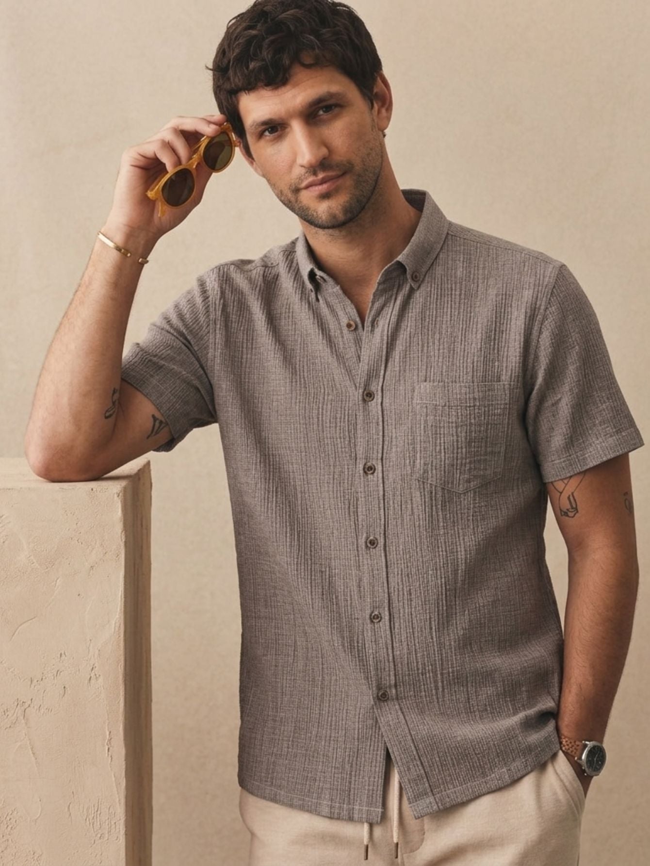 The Breeze Crinkle Shirt in taupe — relaxed short-sleeve button-down with textured fabric, worn by male model against warm neutral background